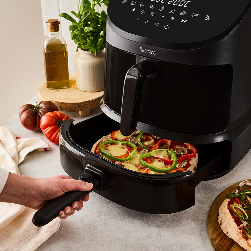 The bottom basket of the Baccarat Air Fryer and Pizza Cooker is being used to cook a pizza. The long handle allows for safe handling after cooking. Select the cooking function on the digital touch panel at the top.