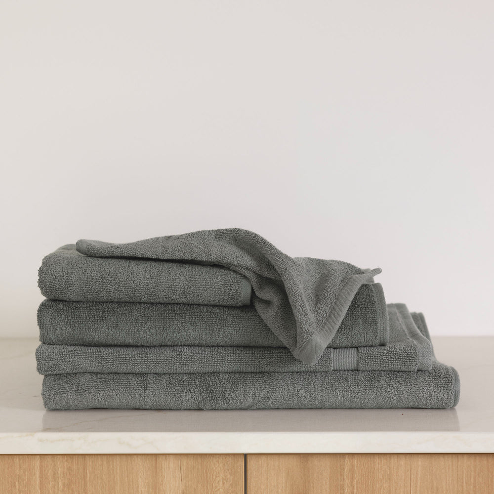The Bambury Chateau Bath range in Charcoal Is folded and stacked displaying the soft texture and colour on the white bench.