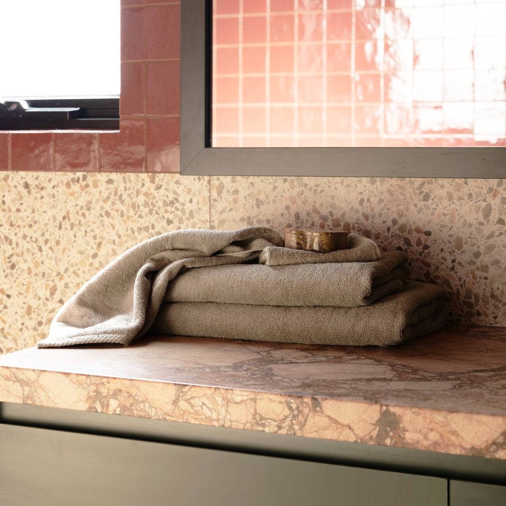 Bambury bath set including the bath mat in the colour latte pictured on a bathroom vanity folded ready for use.