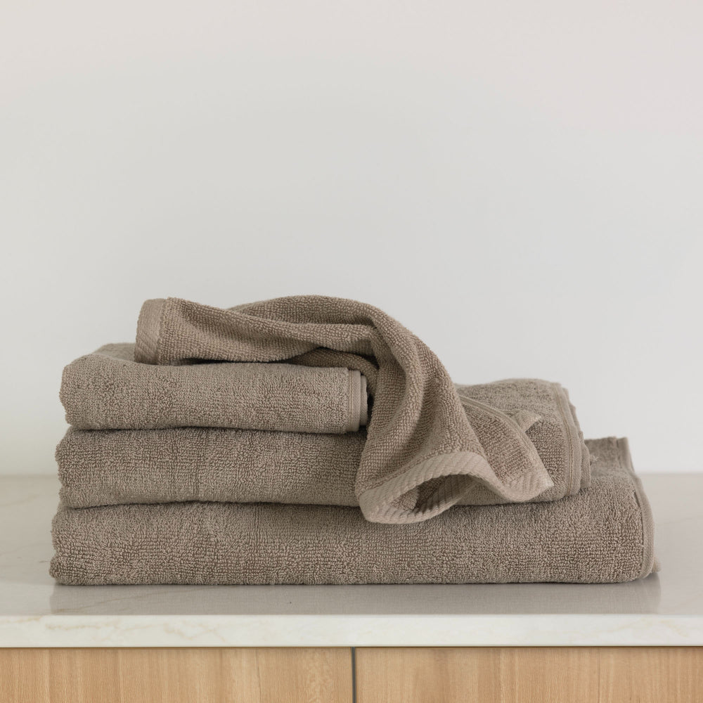 The Bambury Chateau bath range in latte is folded in a pile displaying the items including the bath sheet, bath towel, bath mat, face washer and hand towel.