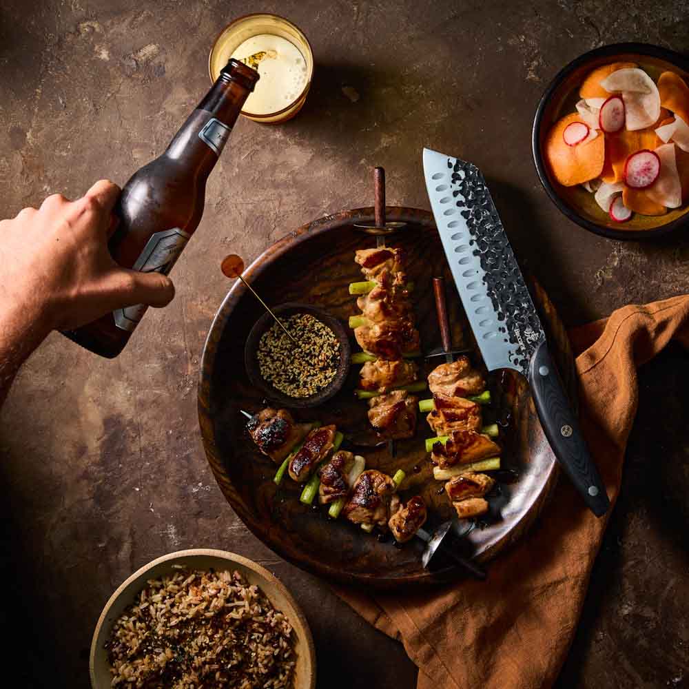 Man pouring beer beside Baccarat KUROI KIBA Santoku Knife 18cm at House