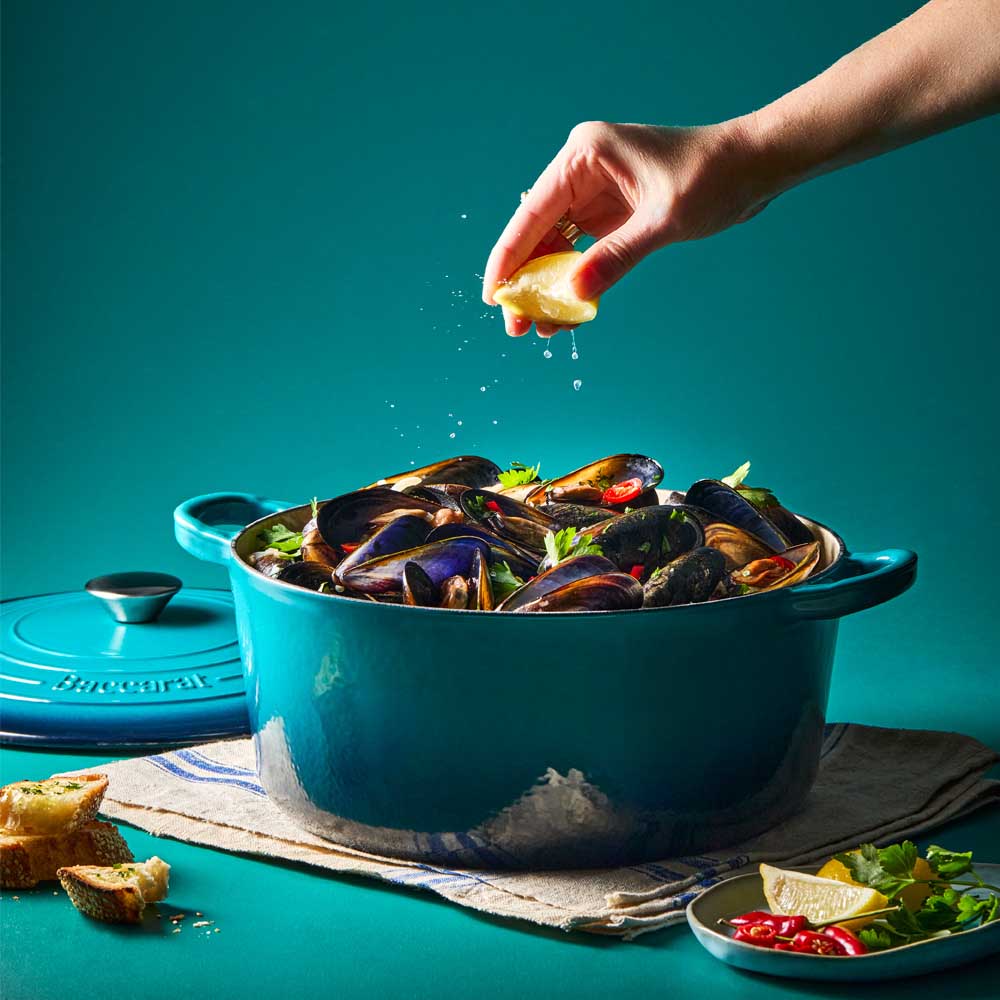 woman squeezing lemon onto blue dutch oven with mussels - House
