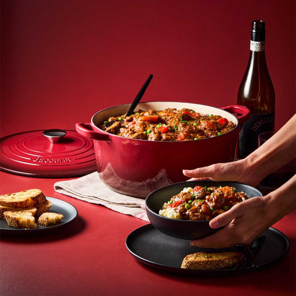 woman serving beef casserole from red dutch french oven - House