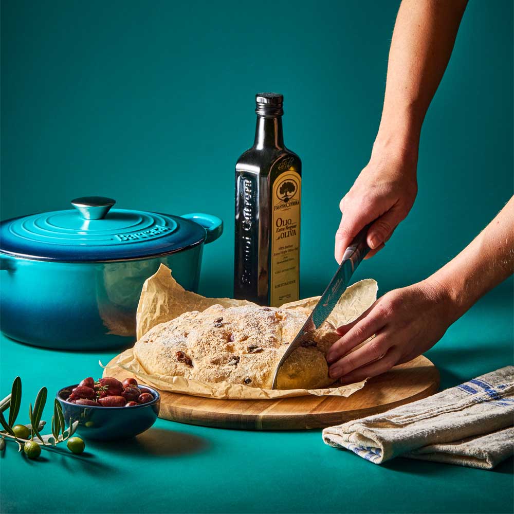 woman cutting bread baked from blue french oven - House