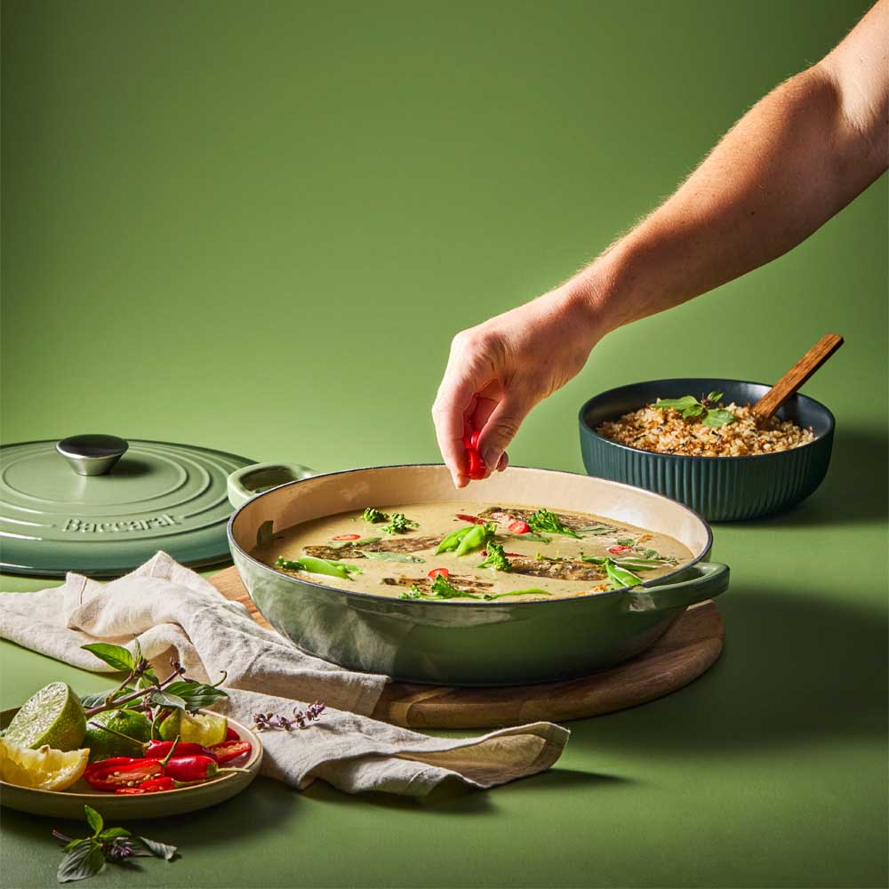 man sprinkling chilli into curry in green saute pan - House