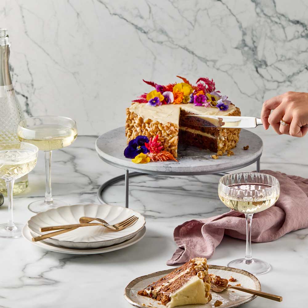 woman cutting slice of cake from marble serving board with stand - House