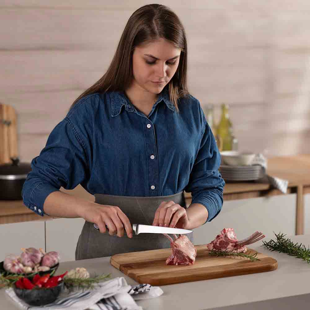 woman frenching rack of lamb with boning knife - House