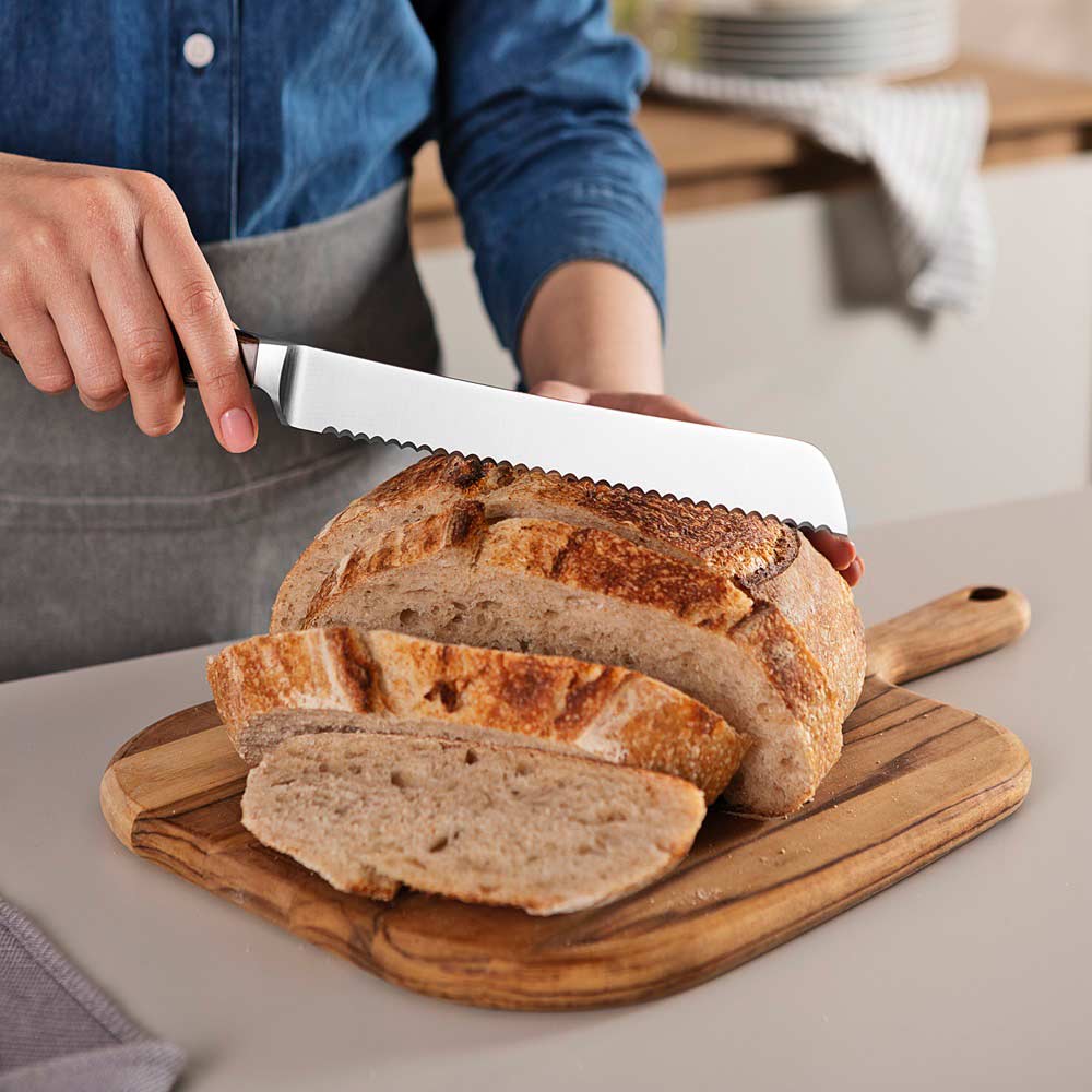 woman cutting slices of bread with bread knife at kitchen bench - House