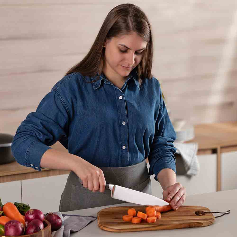 woman chopping carrot at kitchen counter with chef knife - House