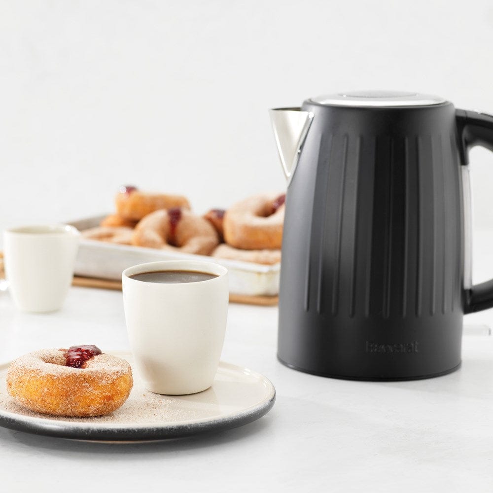 Baccarat The Boiling Point Kettle in Black at House. Black kettle on a kitchen bench with a serve of doughnuts and coffee.