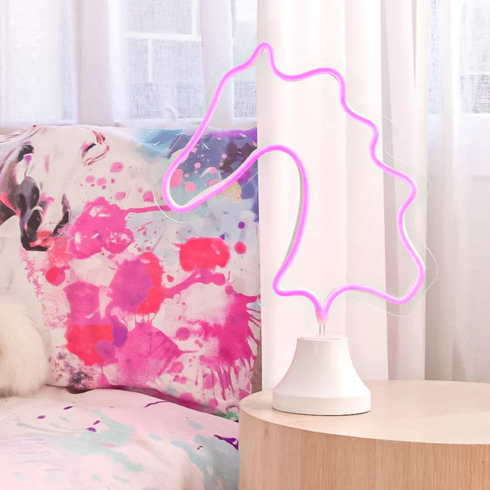 Neon light shaped like a heart on a table with a colorful pillow in the background