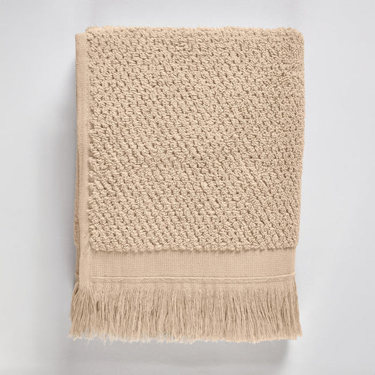 Beige textured bath towel with fringes on a light gray background