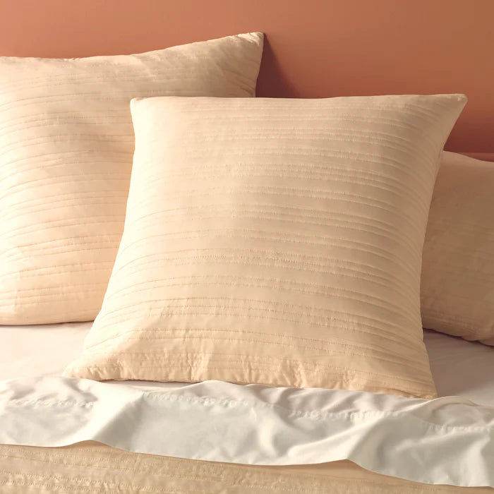 Beige textured pillows on a bed against a peach wall