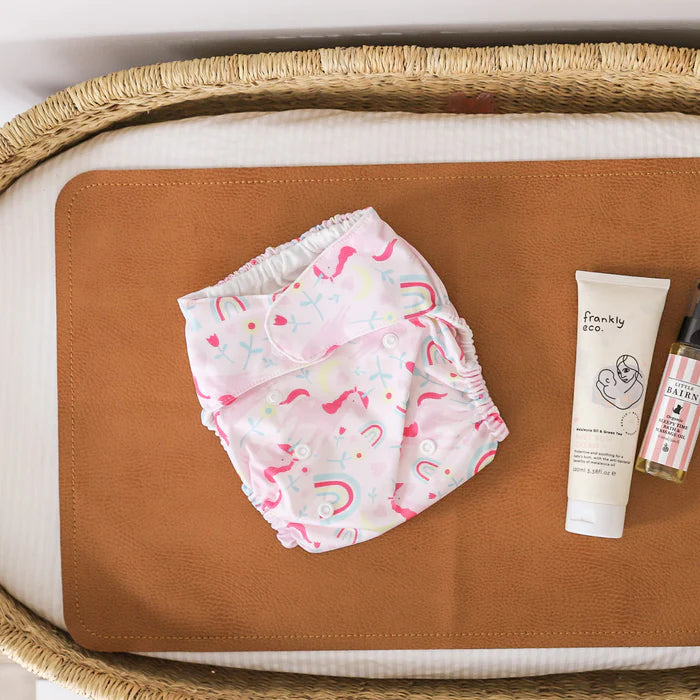 Baby diaper with colorful design on a brown surface, next to a tube of cream and a bottle.