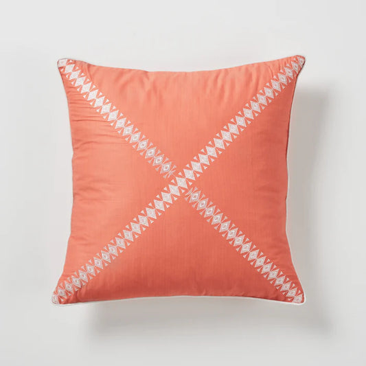 Coral pillow with white geometric pattern on a light gray background