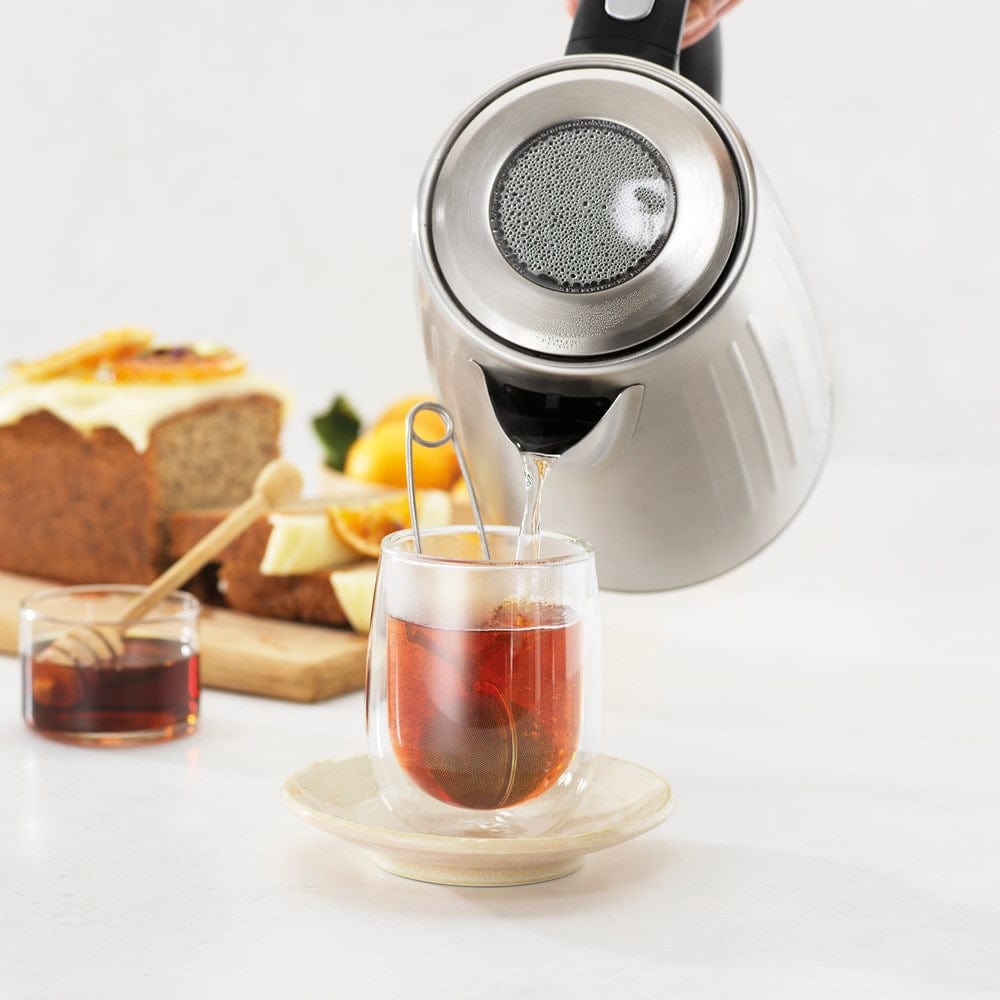 Baccarat The Boiling Point Kettle in Silver at House. Water poured from silver kettle into glass cup with tea